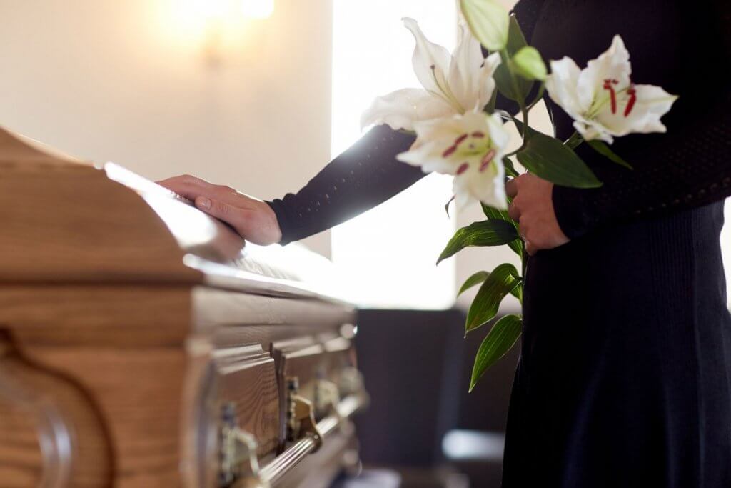 Woman giving simple lily flowers as a gift at a wake by a brown casket