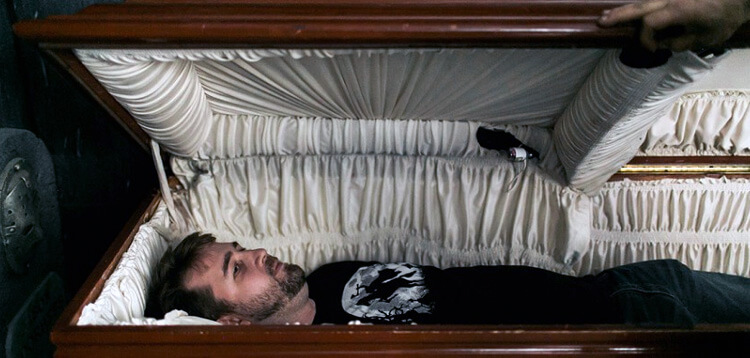awake man lying in casket looking uncomfortable and uncertain